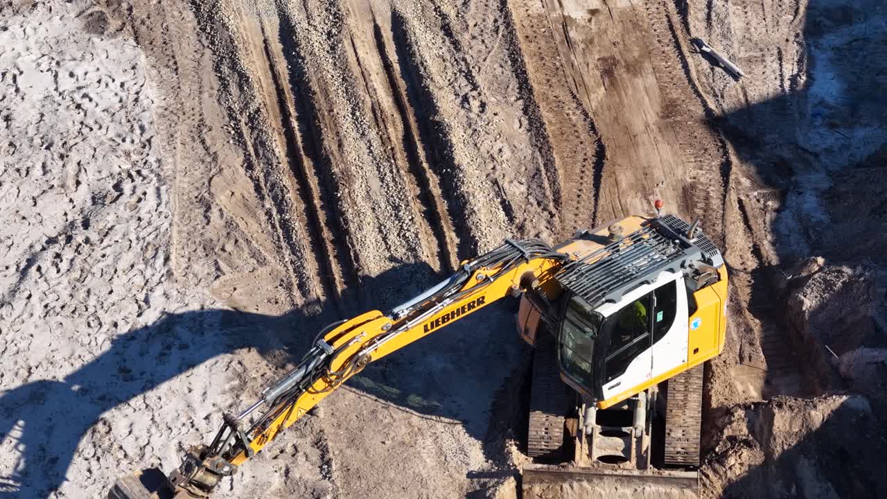 Yellow excavator operates on dirt, digging and moving soil, captured from overhead in bright sunlight