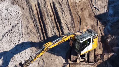 yellow excavator operates on dirt, digging and moving soil, captured from overhead in bright sunlight