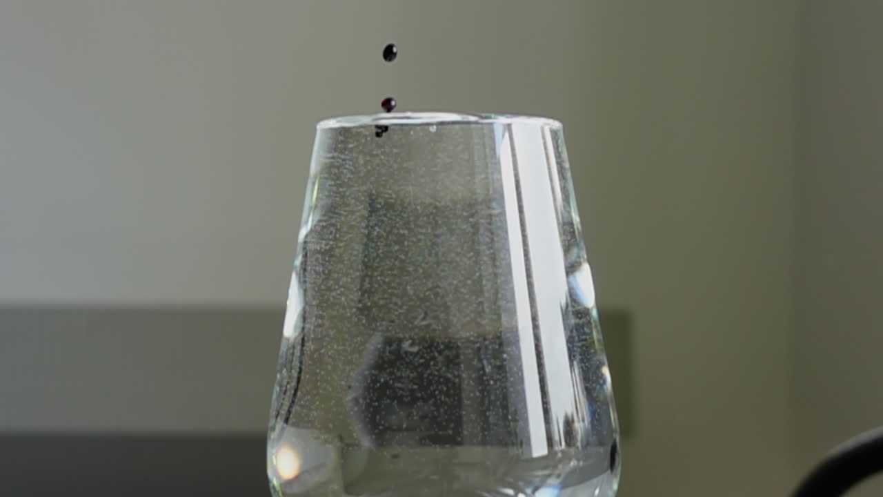 물로 가득 찬 유리잔에 떨어지는 색의 액체 방울 - 느린 움직임 근접