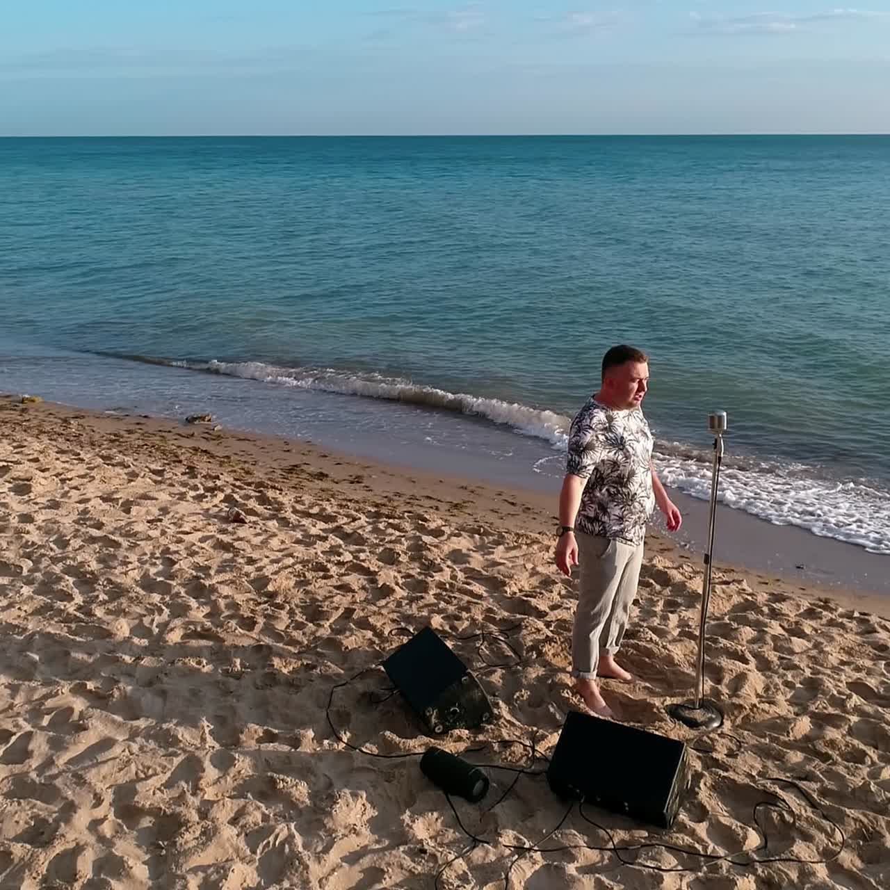 Male singer on a sea beach in summer. Musician standing on a sand shore and singing alone on a beautiful background of sea nature in sunny day
