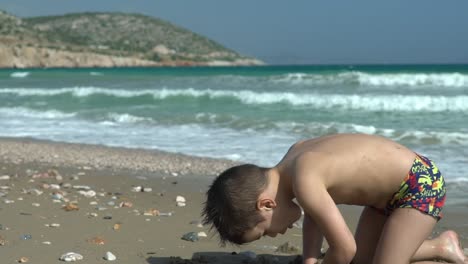 caucasian toddler boy, playing with sand at beach of varkiza, greece