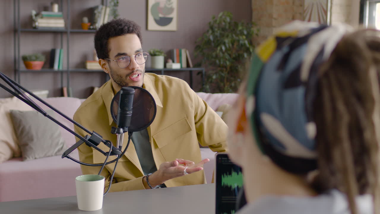 hombre hablando por un micrófono con una mujer sentada en el escritorio con una laptop con ecualizador en la pantalla 1