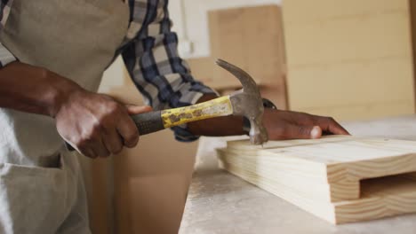 mid section of african american male carpenter hammering nails into the wood at a carpentry shop