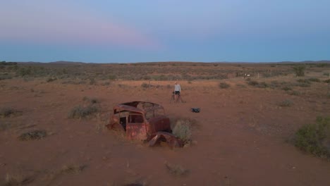 aerial orbit view male photographer taking photos of old rusty abandoned car on outback