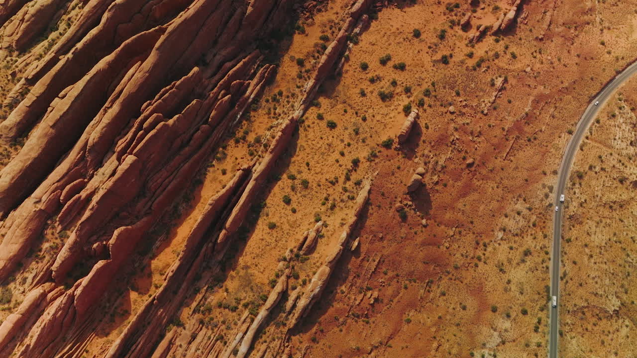 Cars driving by the road going along strangely shaped rocks. Orange desert with canyons in Utah, USA. Aerial view.