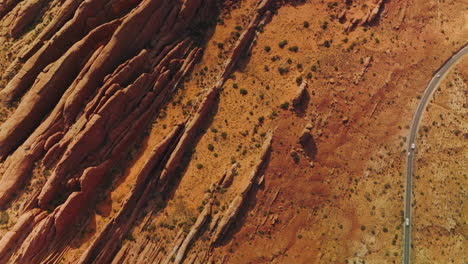 cars driving by the road going along strangely shaped rocks. orange desert with canyons in utah, usa. aerial view.
