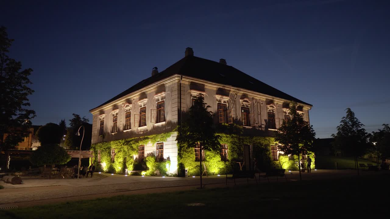 밤에 주변에 몇 사람과 함께 정원에 식물로 덮인 멋진 조명의 오래된 집