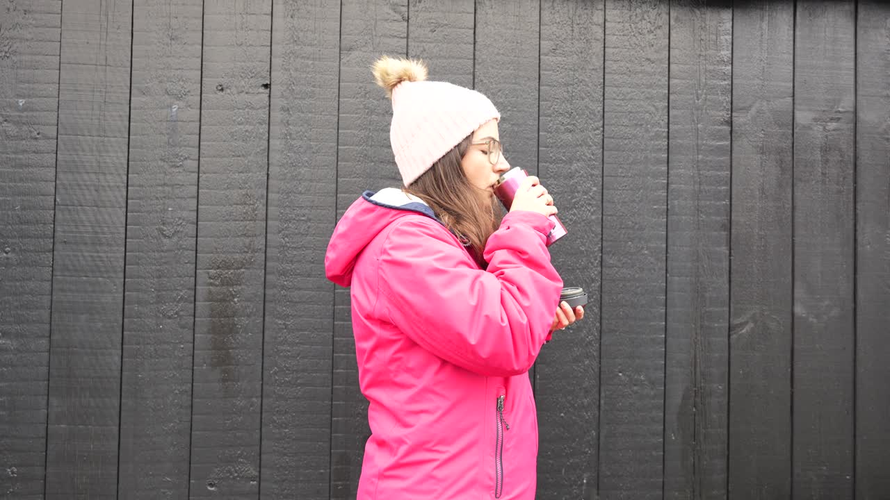 Medium close-up of woman wearing pink rain jacket drinks warm coffe, cold winter