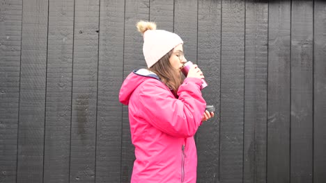 medium close-up of woman wearing pink rain jacket drinks warm coffe, cold winter