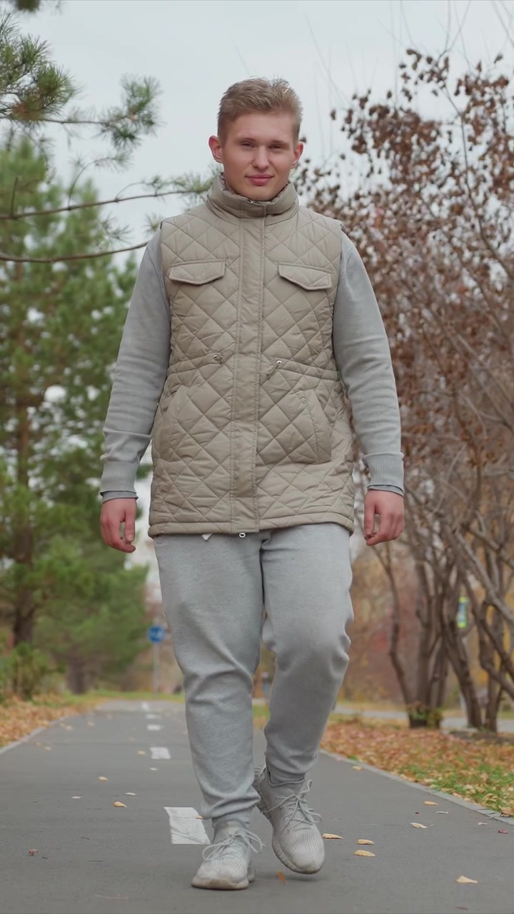 Eine Person bewegt sich stetig auf einem Wanderweg in einem Herbstpark. Das Filmmaterial zeigt Beinbewegungen auf verstreutem Pflaster. Die Outdoor-Szene umfasst kahle Äste einer herbstlichen Baumreihe.