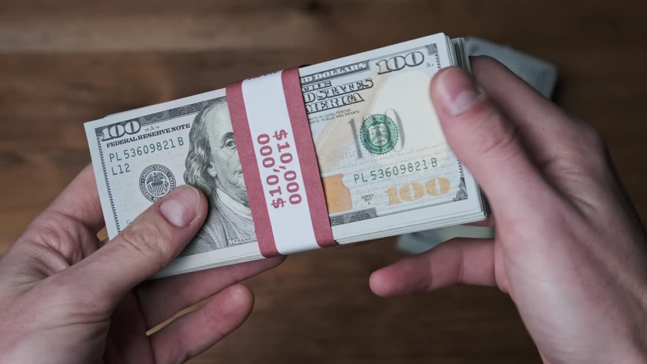 una pila de billetes de 10.000 dólares estadounidenses en manos masculinas sobre un fondo de madera.