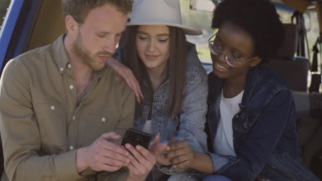 a young male showing his cellphone to two beautiful young girls inside the caravan during a roadtrip 2