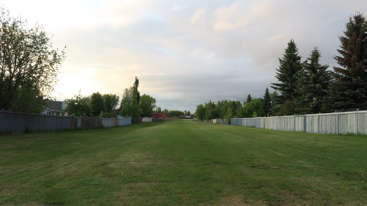 Features a small strip of grassy field separating 2 residential areas. With a cloudy sky and a small window of sunlight.