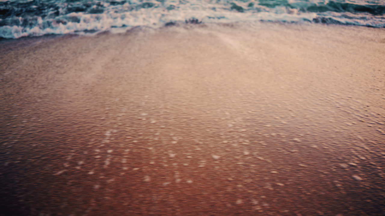Close up of small ocean waves gently rolling onto the sandy beach at sunset
