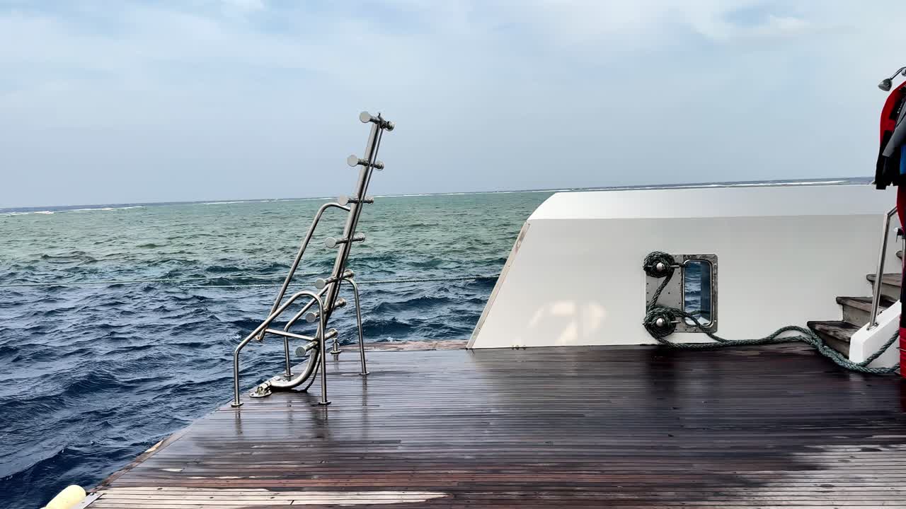 Üppiges azurblaues Meer trifft auf goldene Riffgewässer, vom Teakdeck einer Luxusyacht aus gesehen, an einem hellen tropischen Sommertag, aufgenommen aus einem weiten Blickwinkel auf Augenhöhe, der ruhiges maritimes Reisen und unberührte Natur zeigt.