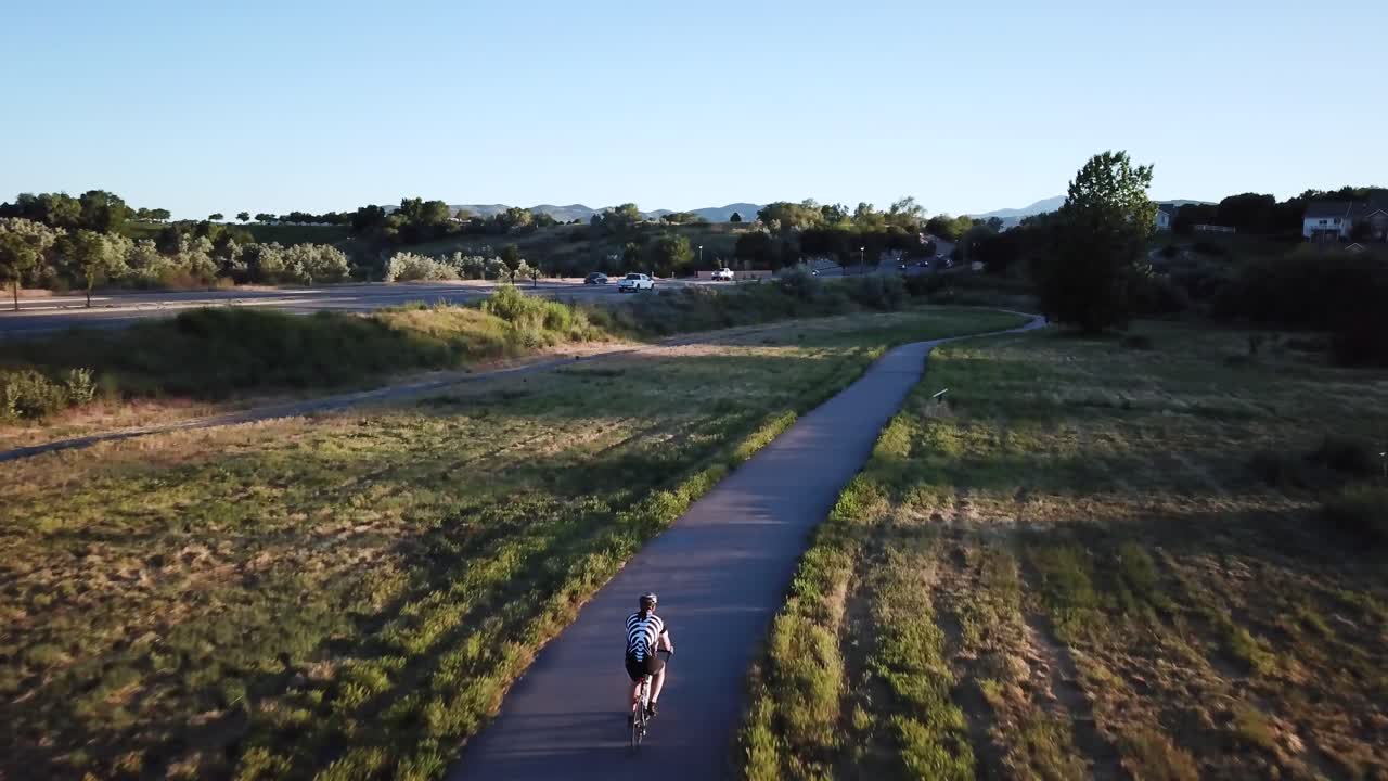 바쁜 도로 근처의 길을 따라 자전거를 타는 자전거 타는 사람을 따라 드론 샷