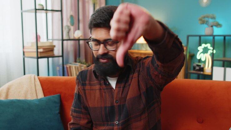 Upset Arabian man showing thumbs down, dislike bad work, disapproval dissatisfied feedback at home