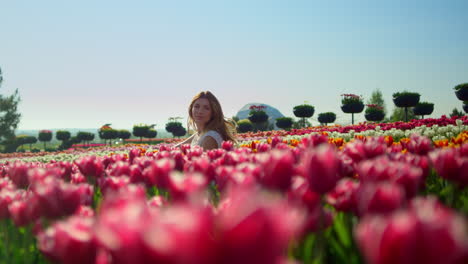 Playful-woman-flirting-in-spring-flower-garden.-View-of-tulip-park-landscape.