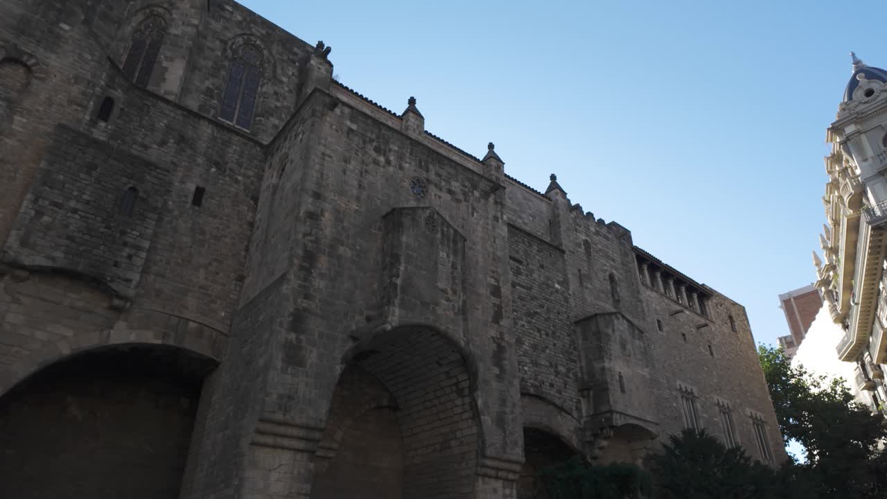 una impresionante vista de las antiguas murallas de la ciudad romana junto a un edificio moderno bajo un cielo azul claro, encarnando la historia y la arquitectura únicas de barcelona.