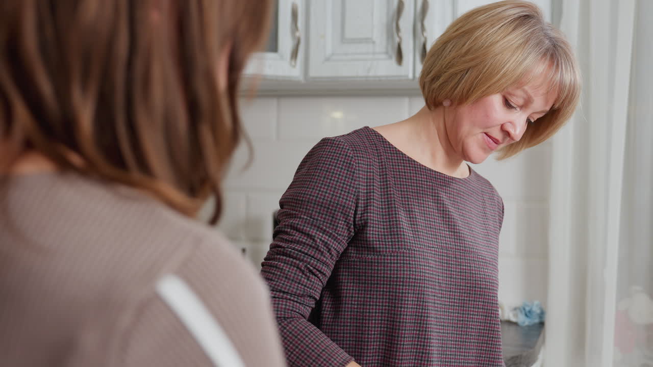 밝은 부에서 요리하는 이모를 관찰하는 동안 책을 들고있는 소녀의 근접 후면 뷰, 이모는 두꺼운 갈색 크리미 으로 비스크를 들어 올리고 준비에 집중합니다.