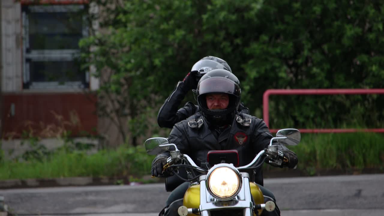 Two motorcyclists on a golden chopper motorbike driving into car park