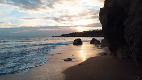 pov walk through hole of cliff reaching sandy beach with waves at algarve at sunset time