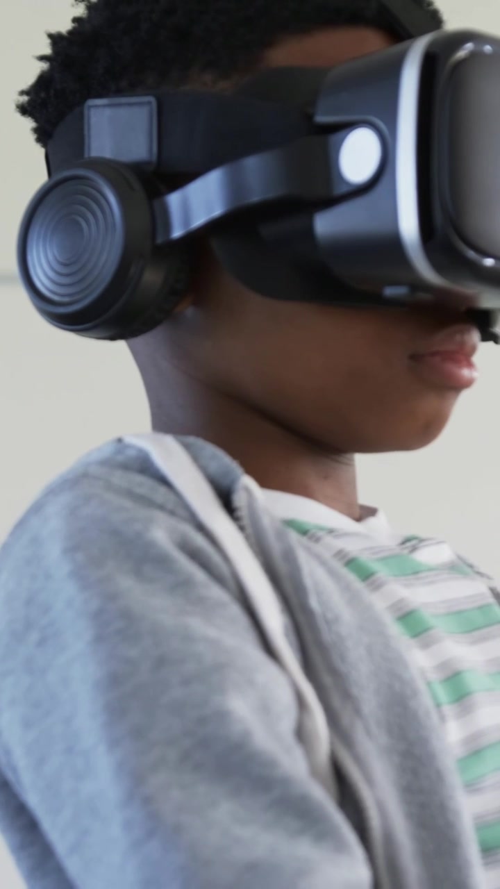 Vertikal video: Ungdom i grå hættetrøje rækker ud og reagerer på et VR-signal, kniber i luften i skolen med et headset.