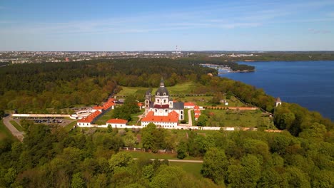 Aerial-shot-of-old-Pazaislis-Monastery-and-Church-and-forest-on-sunny-day-with-blue-clear-sky,-in-Kaunas,-Lithuania,-parallax-shot