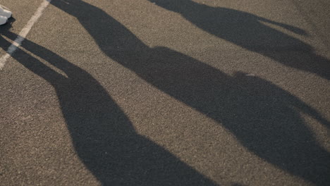 shadow of people jumping cast on ground with partial leg view, one person wearing canvas shoes, the dynamic movement creates a striking visual on the pavement with a distant background