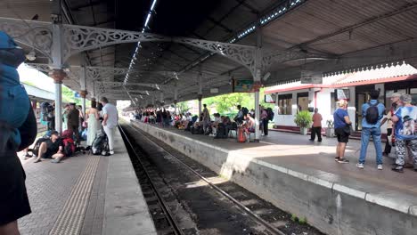 tourists waiting for a train at kandy station, sri lanka. the platform is lively with travelers anticipating their journey, under the station's historic architecture.