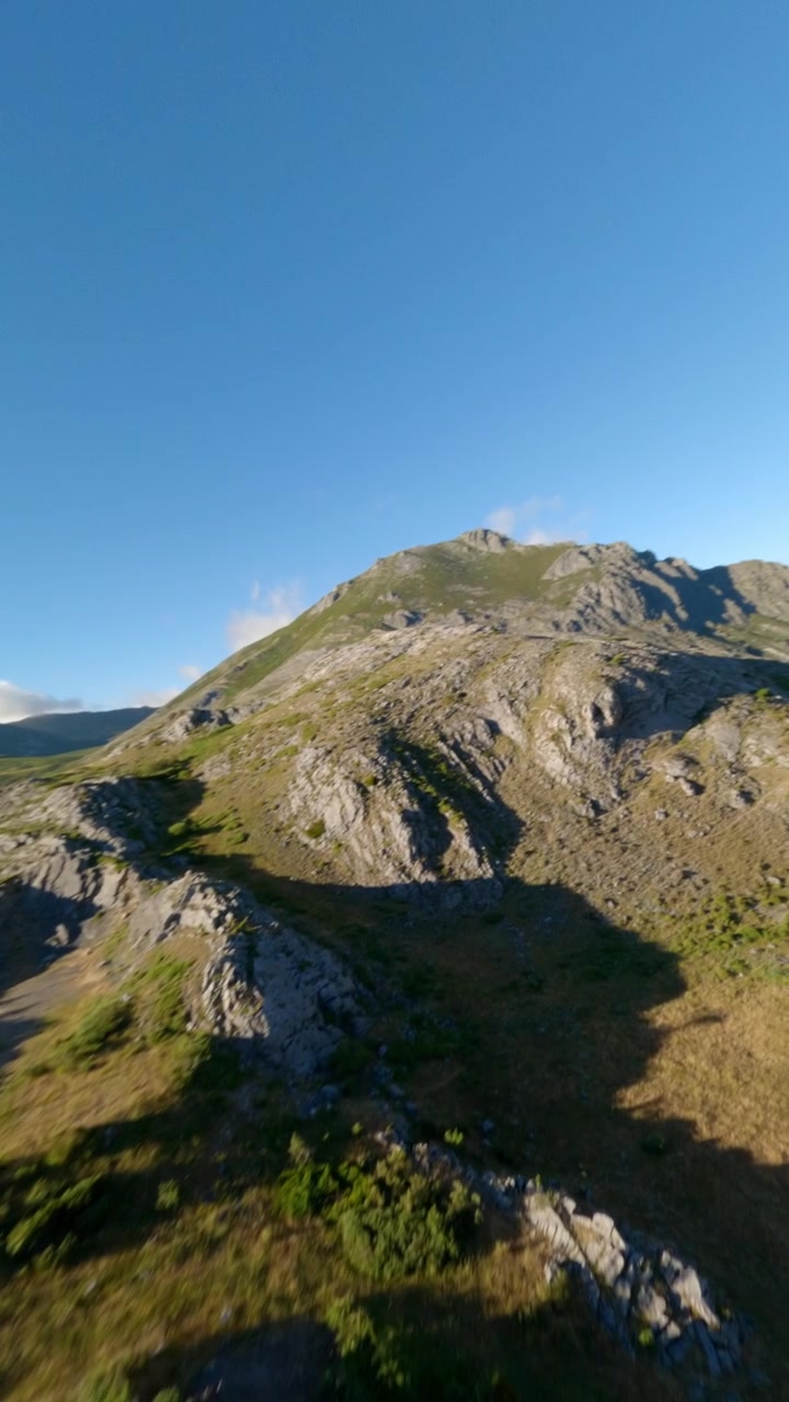 Ripresa dinamica verticale con drone FPV che sorvola creste montuose aspre e un lago blu al tramonto. Cattura l'essenza dell'avventura, del benessere e del viaggio sostenibile nella natura