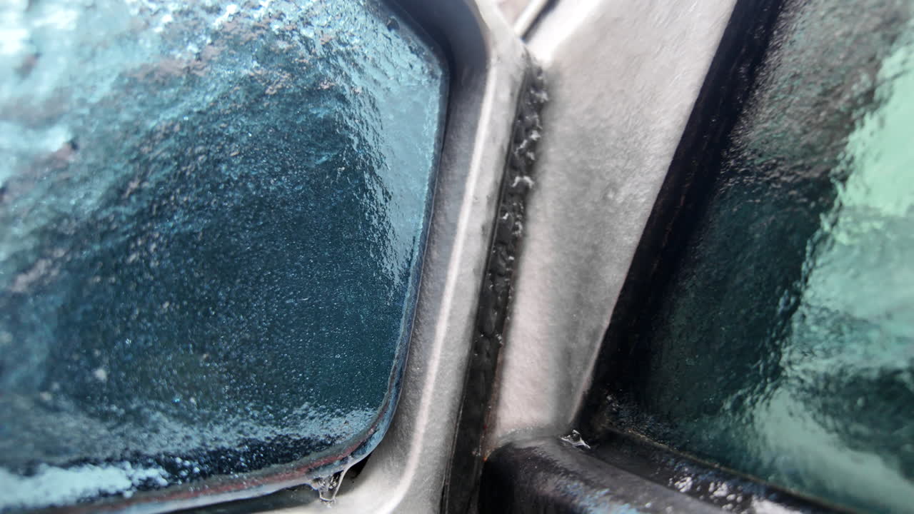 Close up of a car side mirror covered in ice and dripping meltwater