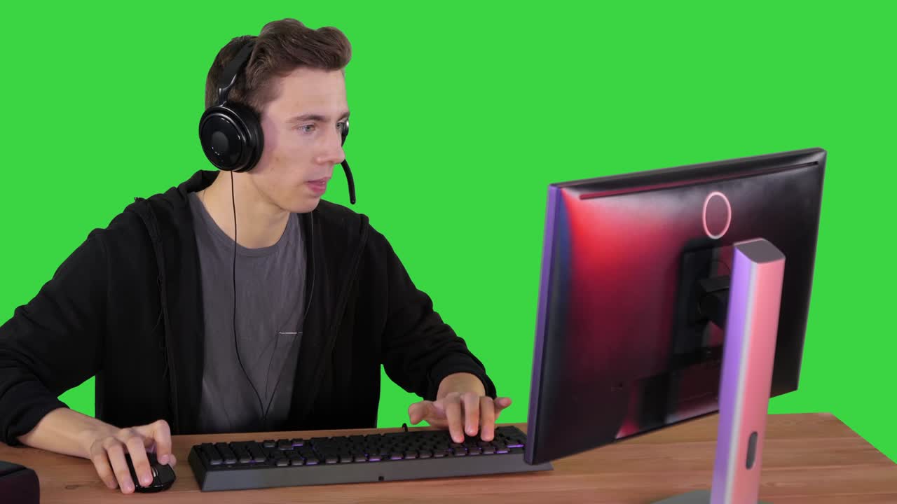 헤드폰을 착용한 게이머가 컴퓨터에서 비디오 게임을 하고 녹색 화면에서 승리합니다.