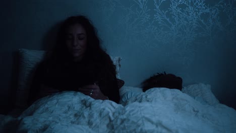 woman watching a tablet device while sitting in bed at night and her partner sleeps