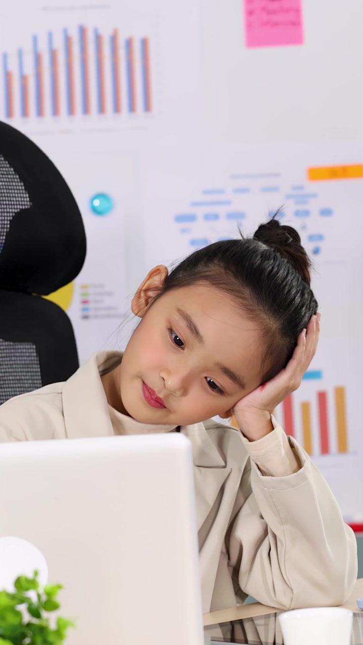 Una giovane ragazza che indossa un blazer appoggia la testa mentre lavora al laptop.