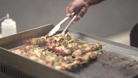 Cook-flipping-chicken-and-vegetable-skewers-on-a-frying-surface,-Close-up-shot