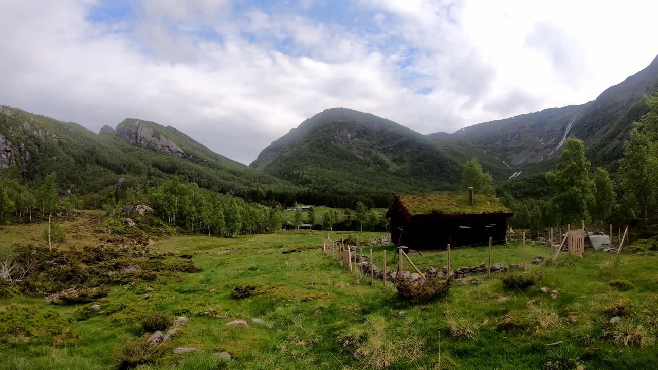 pequeño y acogedor cobertizo exterior con techo de hierba en el idílico valle leiro en eidslandet noruega - lapso de tiempo con hermosas nubes y sombras pasajeras del exuberante paisaje montañoso noruego