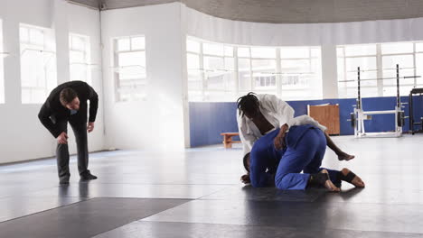 judo athletes practicing grappling techniques in gym with coach observing closely