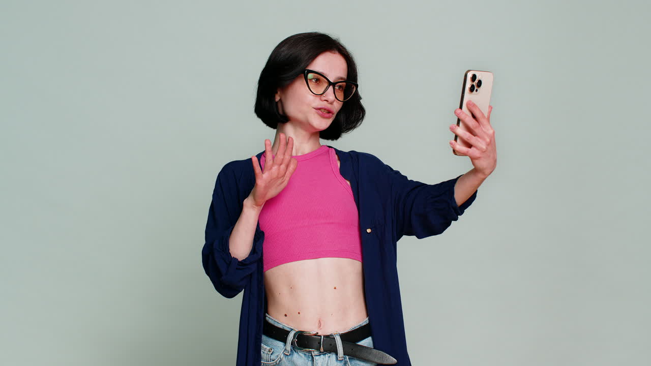 Giovane donna, smartphone alla mano, parla energicamente alla telecamera mentre registra attivamente un vlog, salutando.