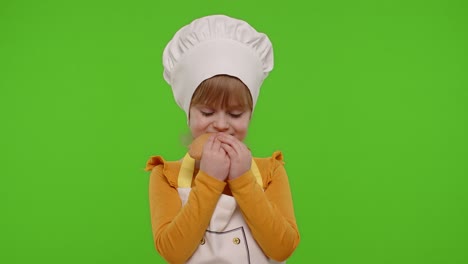 Child-girl-5-6-years-old-dressed-in-apron-like-chef-cook-eating-tasty-bun-on-chroma-key-background