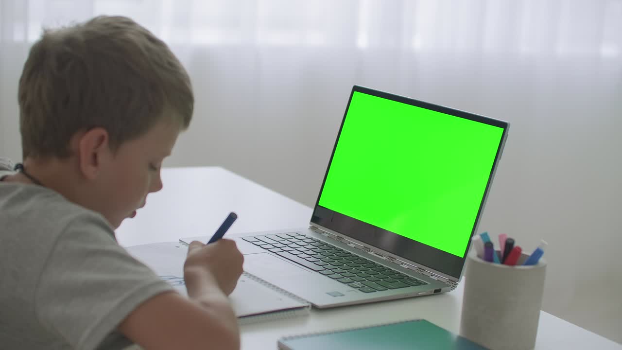 el niño está aprendiendo remotamente, viendo video en la computadora portátil y dibujando en papel con lápiz, pantalla de tecla cromática