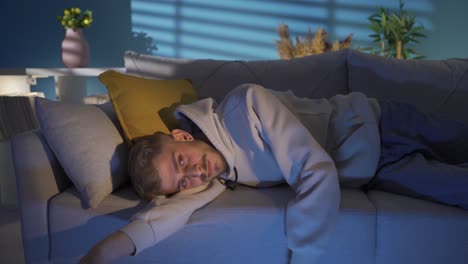 depressed young man lying on sofa at home, thoughtful.