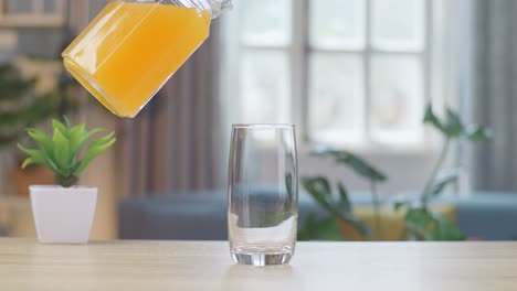 orange juice being poured into a glass on the table at home