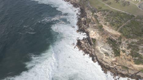 ocean waves crashing against rocky cliffs of dolphins point in gordons bay - coogee beach in sydney, nsw, australia