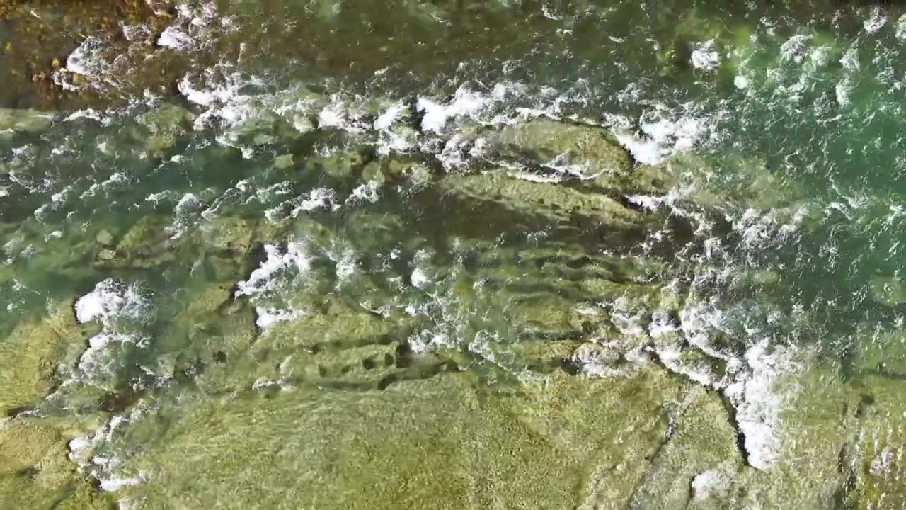 Una ripresa aerea con drone cattura l'acqua verde del fiume che scorre impetuosa su un letto di fiume roccioso e una riva lussureggiante.