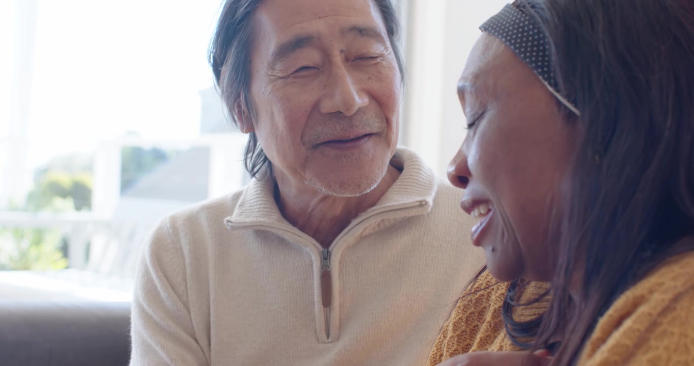 ソファで語り合い、胸に手を当てて寄り添う年配の日本人男性とアフリカ人女性
