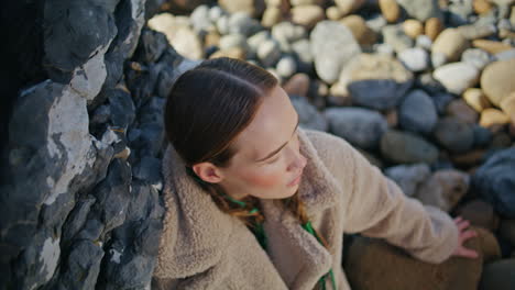 calm traveler resting shore stones closeup. beautiful woman in coat look camera