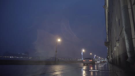 autumn rainy city street at night, night traffic on wet road during rain, street lights reflected in puddles. motion. beautiful embankment and illuminated bridge, first person shooting effect