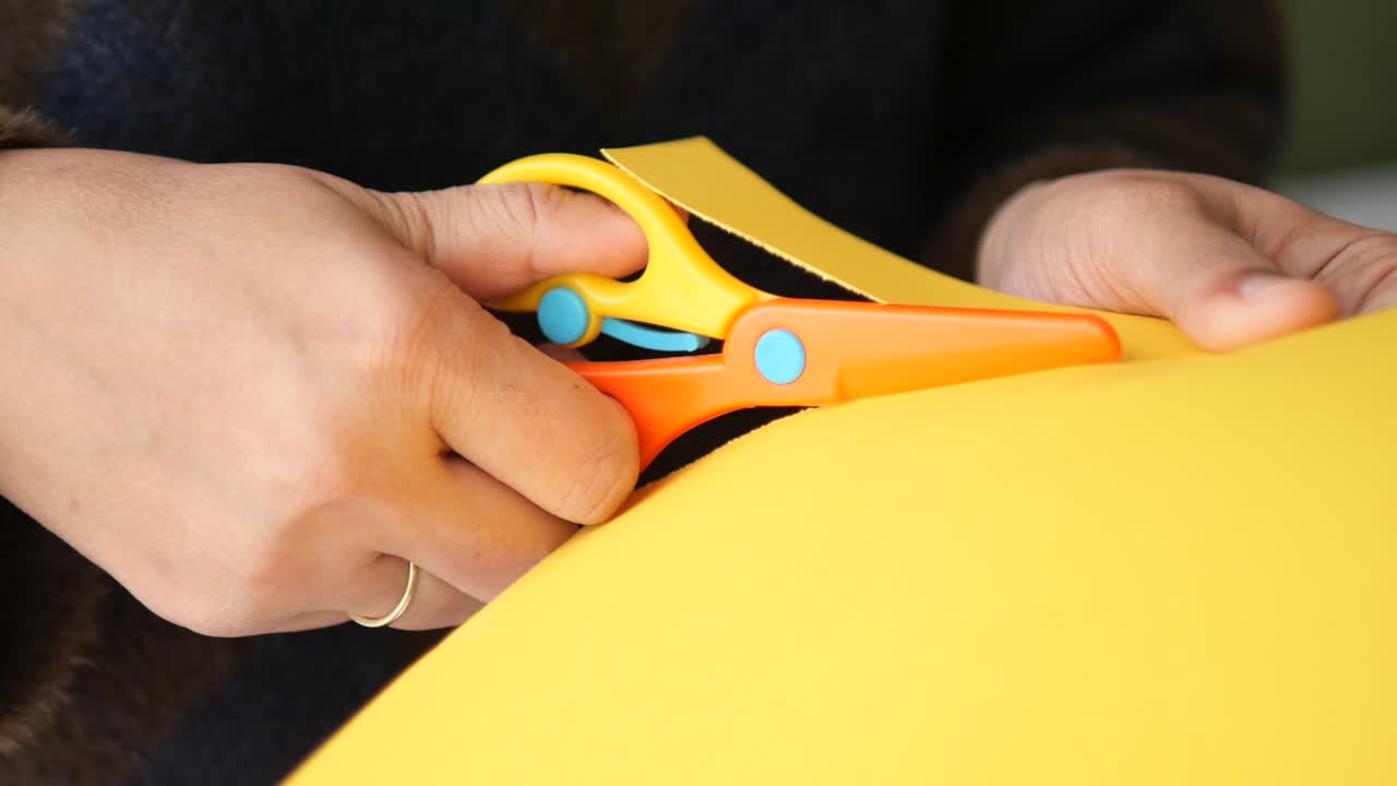 Close-up de Mãos Cortando Papel Amarelo com Tesouras Coloridas.