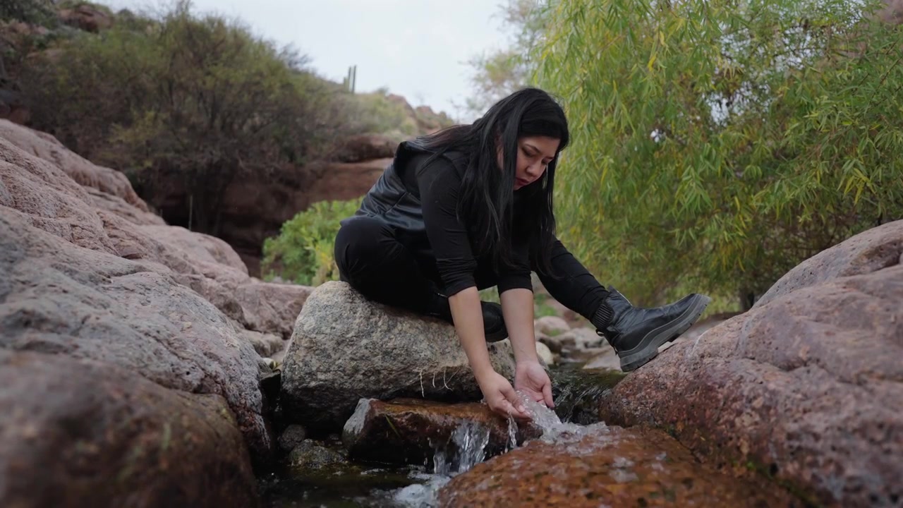 Jovem mulher tocando a água fresca do riacho enquanto sentada em rochas na paisagem natural de cânion da Argentina, demonstrando relaxamento, bem-estar e conexão com a natureza ao ar livre, imagem estática